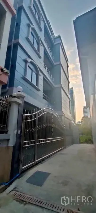 Home Office for rent in Pathum Wan, Bangkok - Blue-grey home office building façade with gated entrance viewed at dusk.