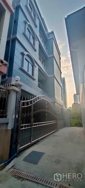 Home Office for rent in Pathum Wan, Bangkok - Blue-grey home office building façade with gated entrance viewed at dusk.