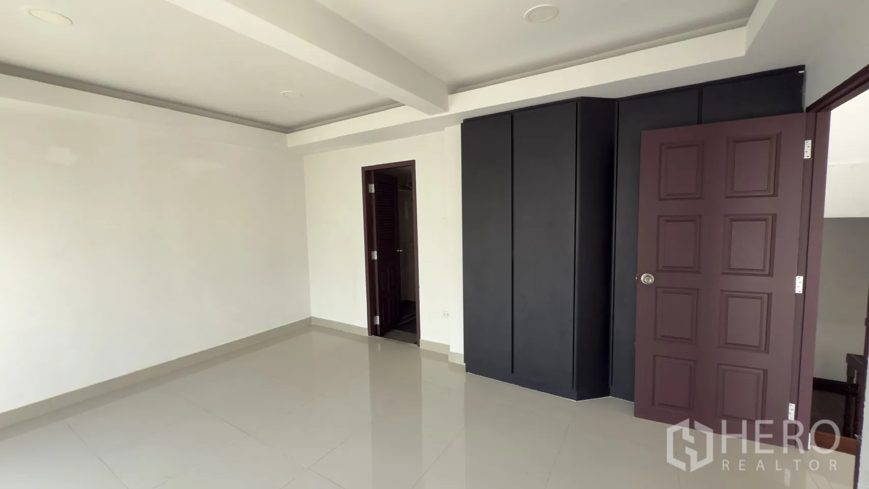 Townhouse for rent in Watthana, Bangkok - Bedroom with a black built-in wardrobe and a doorway to a tiled bathroom.