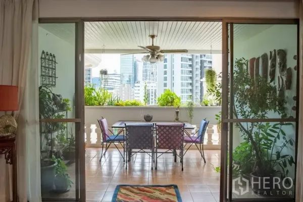 Condominium for rent in Khlong Toei, Bangkok - Covered balcony with sliding glass doors, ceiling fan, potted greenery and skyline view set for alfresco dining.