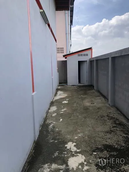 Warehouse for rent in Nonthaburi - Side service alley beside the warehouse with concrete path, boundary wall and a small utility room.
