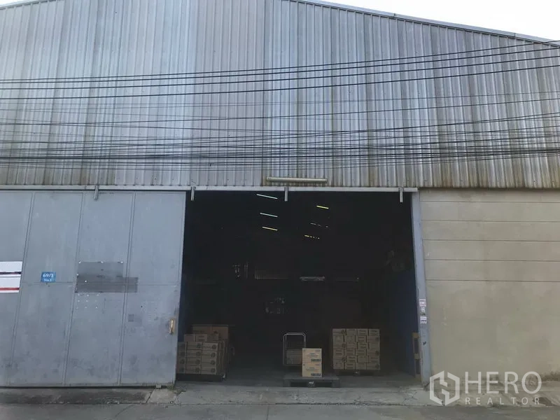Warehouse for rent in Bang Phli, Samut Prakan - Front of an industrial warehouse with large sliding metal doors open, showing stacks of boxes at the loading area.