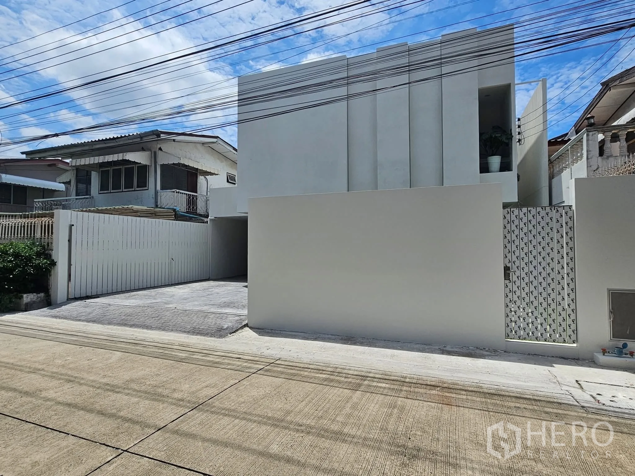 独栋房屋 for sale in Lat Phrao, Bangkok - 房屋白色现代外立面，高墙与入户大门。