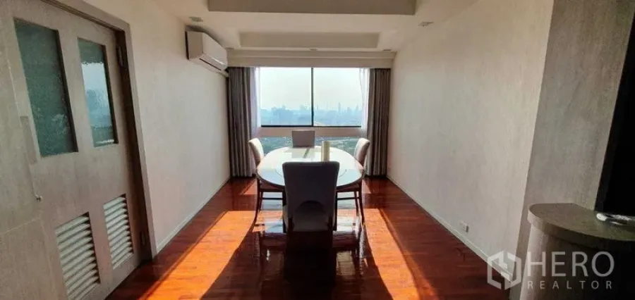 Condominium for rent in Khlong Toei, Bangkok - Dining area with large window, city skyline view, wooden flooring, and air conditioning.