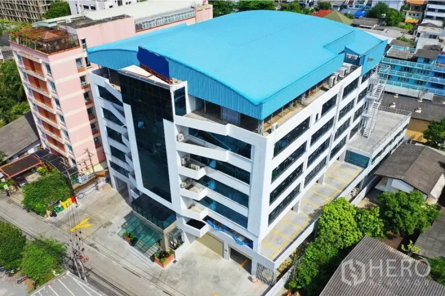 Office Space for rent in Khlong Toei, Bangkok - Aerial view of a modern mid-rise office building with a blue roof and on-site parking in Khlong Toei, Bangkok.