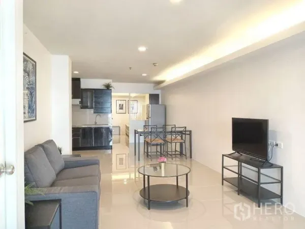 Condominium for rent in Khlong Toei, Bangkok - Long living room view toward the kitchen with TV, sofa and recessed lighting in an 85 sqm Phrom Phong condo.