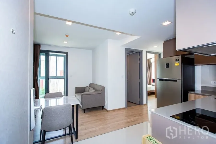 Condominium for rent in Watthana, Bangkok - Bright open-plan living area with sofa, dining table and modern kitchenette with fridge and hob, wood flooring and full-height windows.