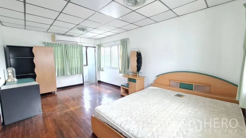 Detached House for rent in Lat Phrao, Bangkok - Large master bedroom with wood floors, green curtains and built-in furniture.