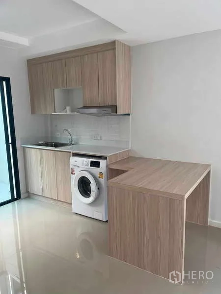 Townhouse for rent in Suan Luang, Bangkok - Modern light-wood kitchenette with cabinets, sink, cooktop, peninsula counter and washing machine.