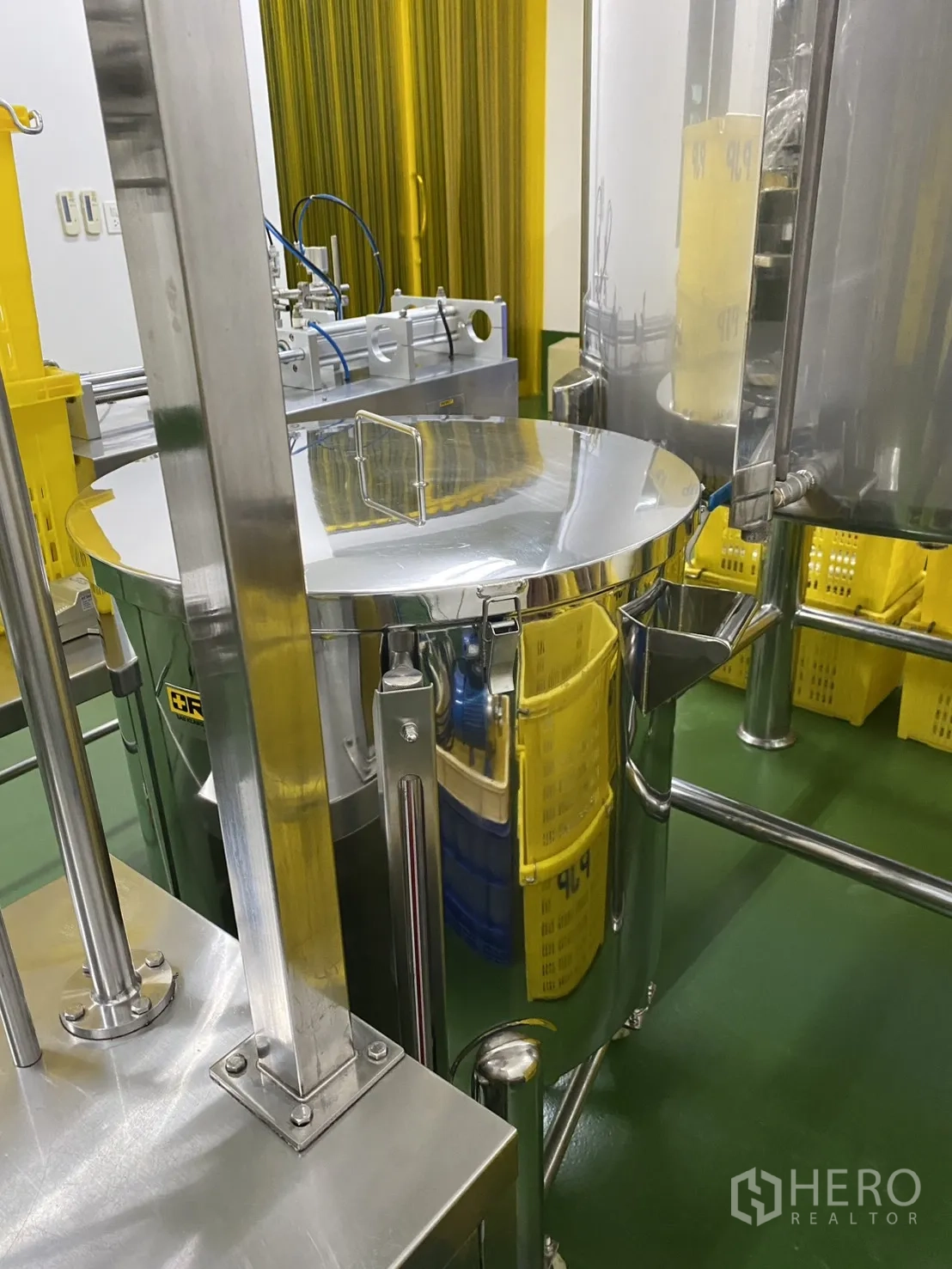 Factory for sale in Khlong Luang, Pathum Thani - Stainless mixing tanks positioned near stacks of yellow crates in a clean area.