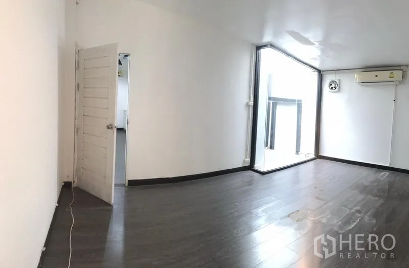 Shophouse for rent in Watthana, Bangkok - Bright shophouse room with dark wood floors, corner glass and wall AC, plus door to an adjoining space.