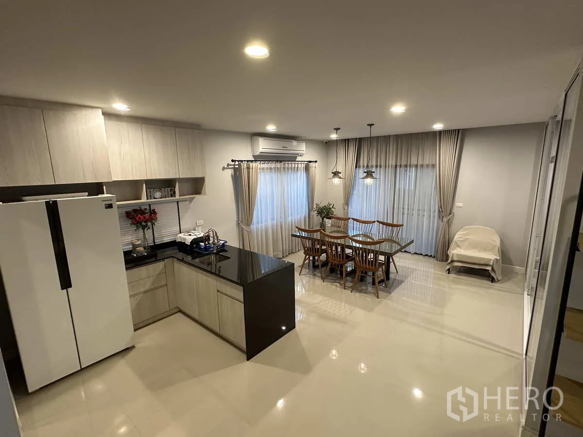 Detached House for rent or sale in Lam Luk Ka, Pathum Thani - Open‑plan kitchen with L‑shaped cabinets, black countertop and dining area.