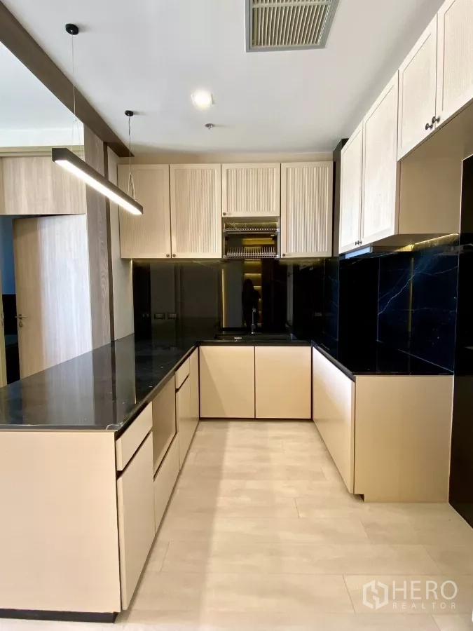 Condominium for sale in Pathum Wan, Bangkok - U-shaped kitchen layout with glossy black backsplash, ample cabinets, and wide countertop.
