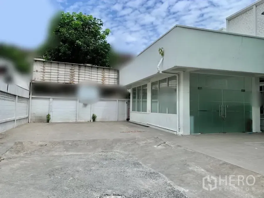 Retail Space for rent in Khlong Toei, Bangkok - Single-storey white commercial building with glass double doors and a wide concrete forecourt for parking and loading.