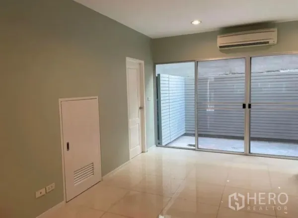 Townhouse for rent in Suan Luang, Bangkok - Air-conditioned living room with glossy tile floors and large sliding glass doors opening to a private patio.