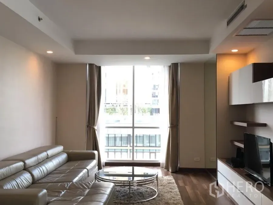Condominium for rent in Pathum Wan, Bangkok - Modern living room with leather sofa, TV unit and floor-to-ceiling window.