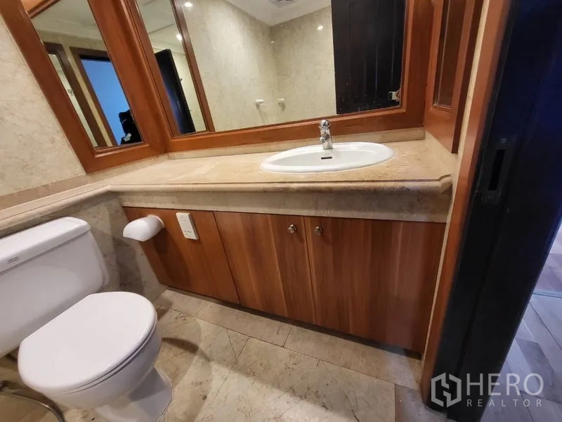 Condominium for rent in Pathum Wan, Bangkok - Bathroom with long stone vanity, framed mirror and toilet on tiled floor.