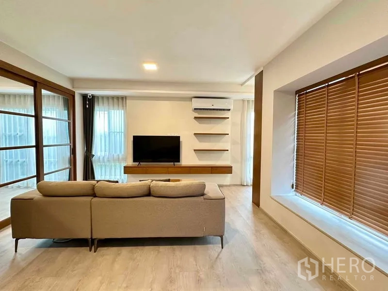 บ้าน ให้เช่าหรือขายในPrawet, Bangkok - ห้องนั่งเล่นสว่าง โซฟาเข้ามุม ทีวีติดผนัง ชั้นลอย แอร์ และหน้าต่างขนาดใหญ่พร้อมผ้าม่าน
