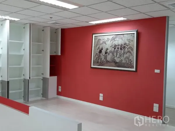 Office Space for rent in Bang Rak, Bangkok - Fitted office area with red feature wall, framed art and open white storage cabinets.