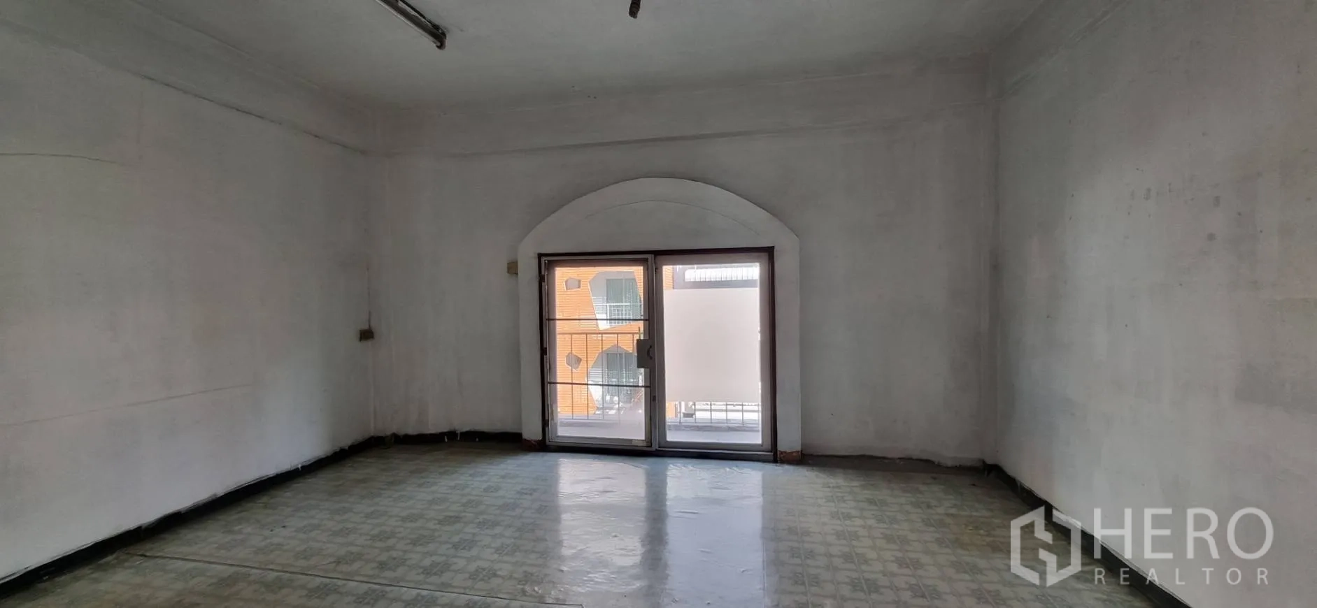 Shophouse for rent or sale in Bangkok - Large empty room with an arched window and patterned vinyl flooring.