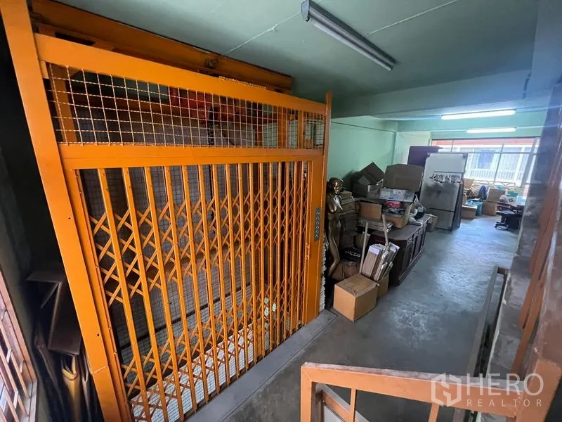 店屋 出租或出售在Watthana, Bangkok - 工业货梯配橙色折叠门，旁为仓储空间与纸箱。