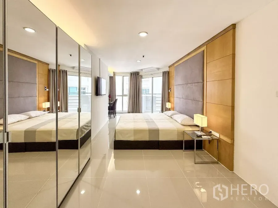 Condominium for rent in Khlong Toei, Bangkok - Bright master bedroom with mirrored wardrobes, padded headboard and sliding glass to the balcony.