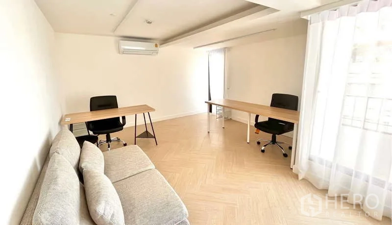 Office Space for rent in Watthana, Bangkok - Compact office area with two desks, a sofa, and sheer curtains allowing daylight.