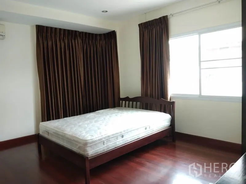 Detached House for rent in Watthana, Bangkok - Bedroom with wooden bed frame, large window, dark curtains and wood flooring.