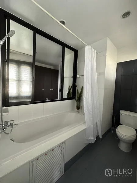 Condominium for rent in Khlong Toei, Bangkok - Bathroom with soaking tub, shower, toilet, and louvered window.