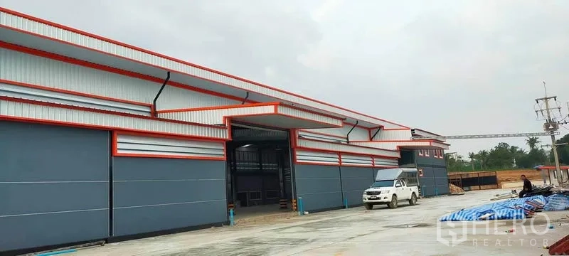 Factory for rent or sale in Phanat Nikhom, Chon Buri - Long facade of the factory with multiple loading doors and a pickup truck on the apron.