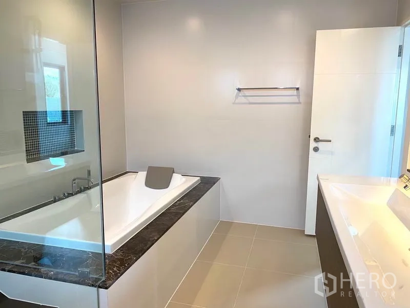 Detached House for rent in Saphan Sung, Bangkok - Modern bathroom with built-in bathtub, glass partition and tiled walls.