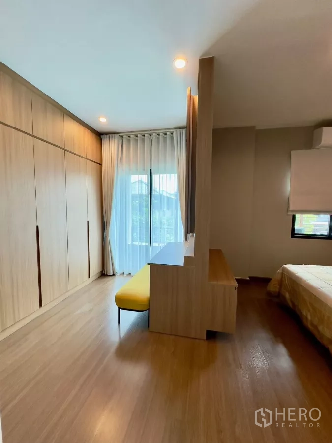 Detached House for rent in Samut Prakan - Dressing area with full-height wardrobes, balcony door and yellow bench.