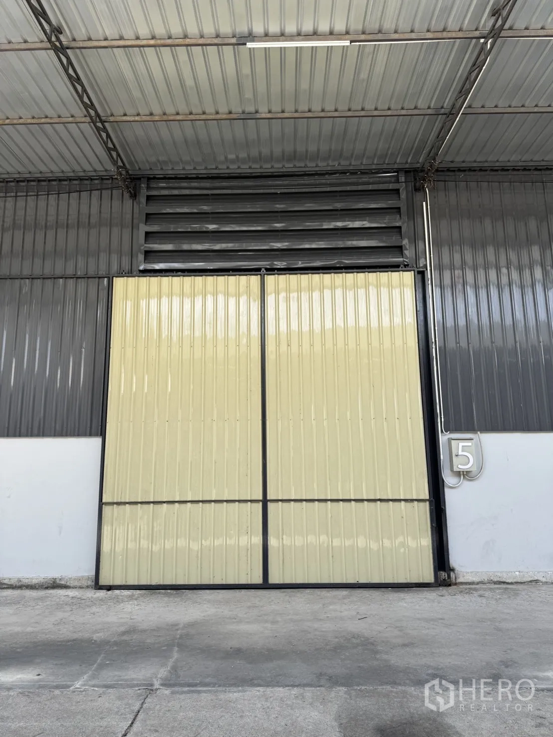 Warehouse for rent in Phra Nakhon Si Ayutthaya, Phra Nakhon Si Ayutthaya - Large sliding metal warehouse door under a covered canopy with ventilation louver and truck-friendly driveway.