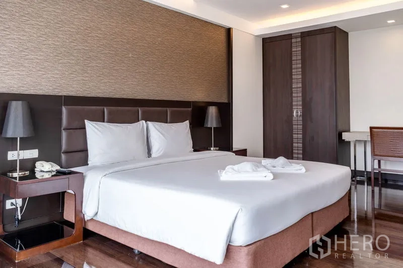 Apartment for rent in Khlong Toei, Bangkok - Master bedroom with king bed, padded headboard, bedside lamps and wardrobe.