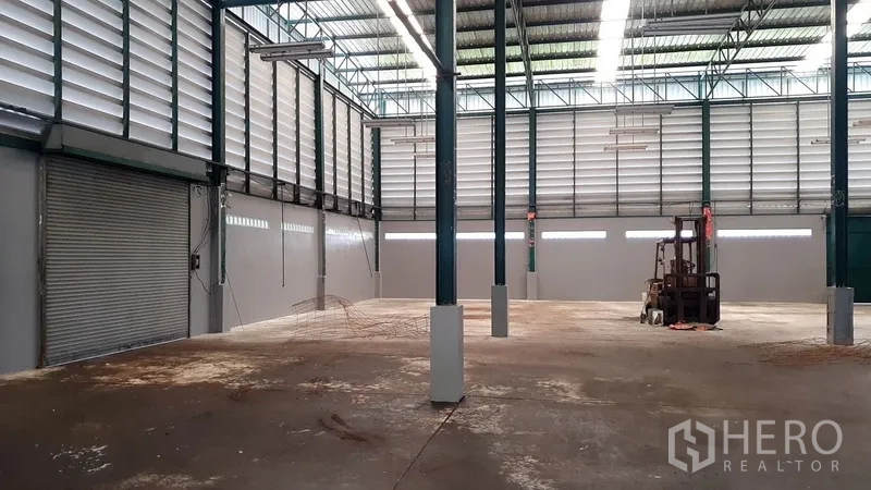 Factory for rent in Saphan Sung, Bangkok - Spacious warehouse bay with high roof, louvered walls, roller shutter doors and a forklift.