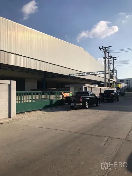 Warehouse for rent in Samut Prakan - Street view of a modern warehouse exterior with metal cladding, secure green gate, and covered loading area in Bang Sao Thong.