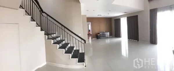 Condominium for rent or sale in Pathum Wan, Bangkok - Spacious duplex living area with tiled floors, a sleek staircase, and large curtained windows.