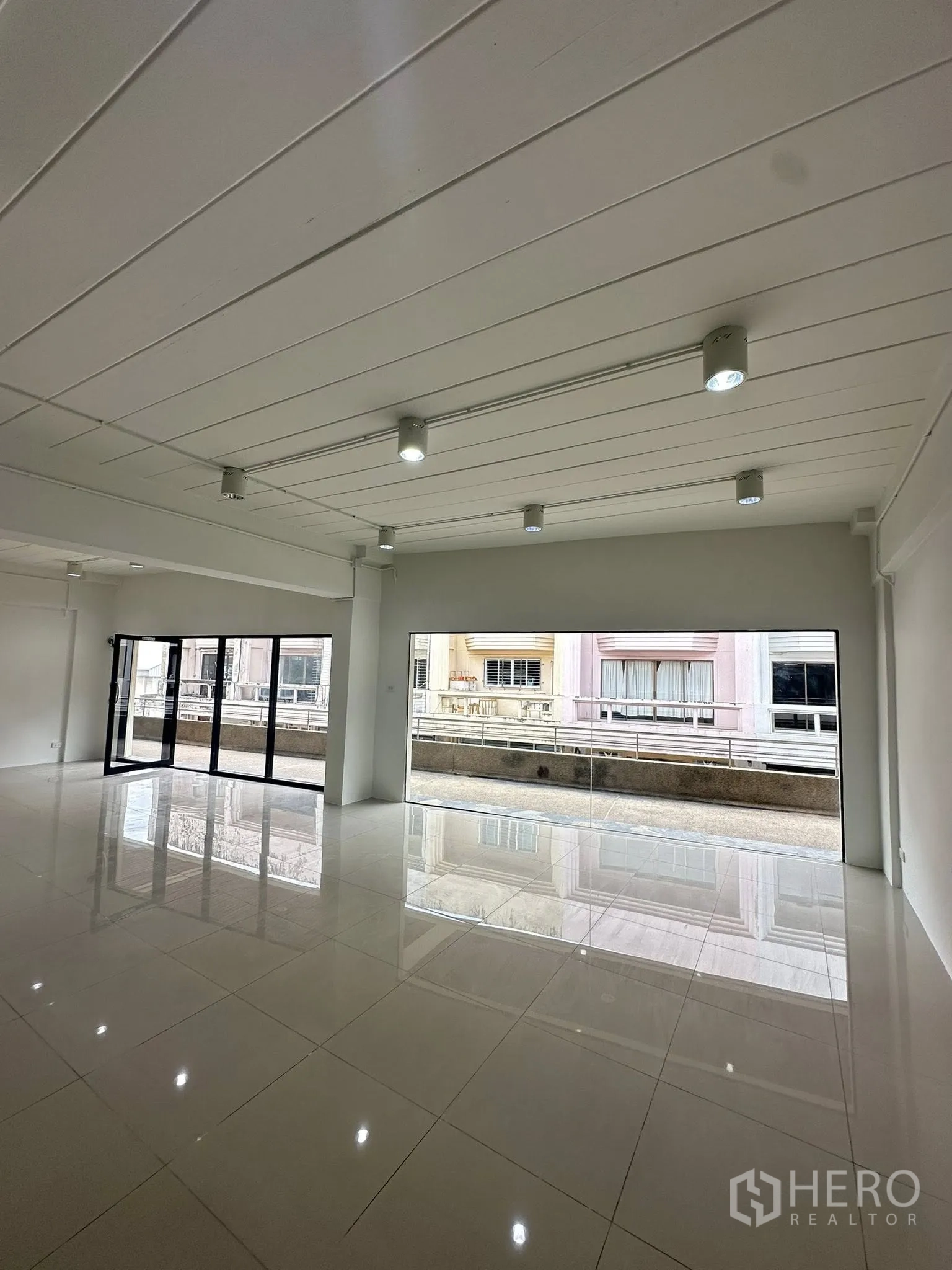 Office Space for rent in Watthana, Bangkok - Sunlit office with full-width windows and folding doors overlooking neighboring blocks.