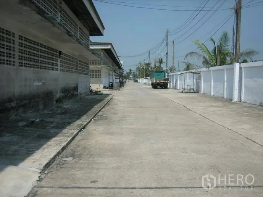Warehouse for rent in Min Buri, Bangkok - Wide concrete access road inside an industrial compound with warehouse blocks, power lines and a parked truck.