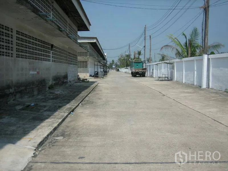 Warehouse for rent in Min Buri, Bangkok - Wide concrete access road inside an industrial compound with warehouse blocks, power lines and a parked truck.