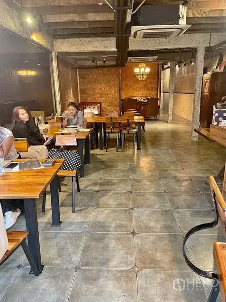 Retail Space for rent in Phaya Thai, Bangkok - Industrial-style dining area with wooden tables, tiled flooring, exposed ceiling beams and chandelier lighting in a compact Ari retail space.