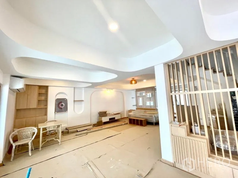 Townhouse for rent in Khlong Toei, Bangkok - Bright open-plan living room with curved ceiling panels, wood slat divider and built-in storage.