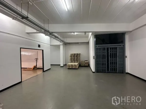 Warehouse for rent in Khlong Sam Wa, Bangkok - Ground‑floor loading zone with a goods lift and pallet jack under bright lighting.