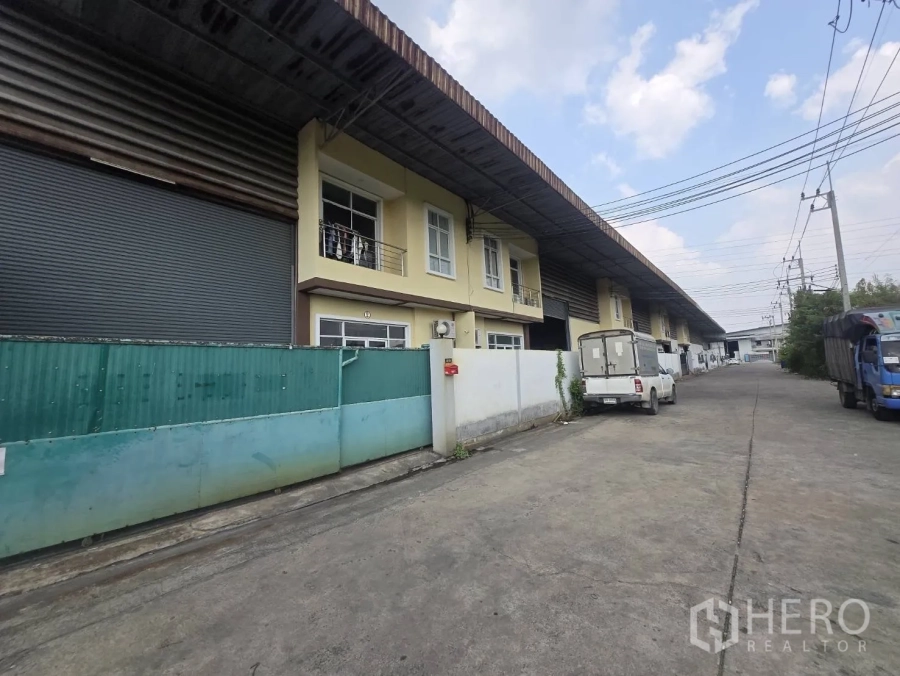 Factory for rent or sale in Mueang Samut Sakhon, Samut Sakhon - Row of factory units along a wide concrete access road with loading and parking areas.