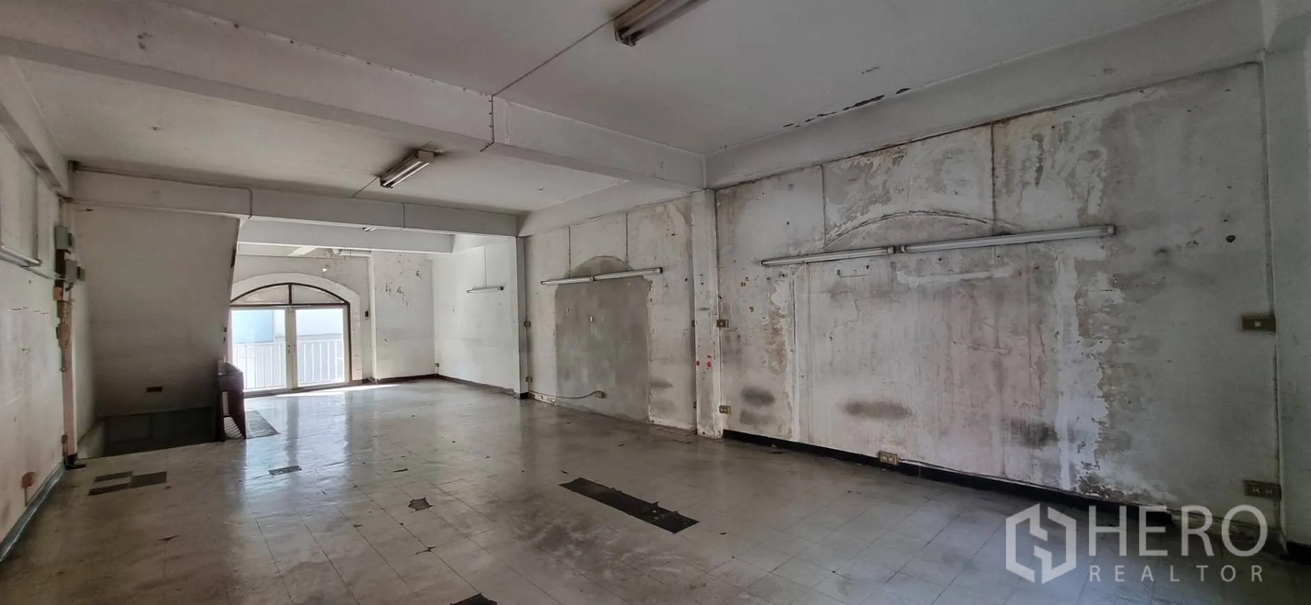 Shophouse for rent or sale in Bangkok - Long hall-style room with worn walls, fluorescent lights and an arched window.