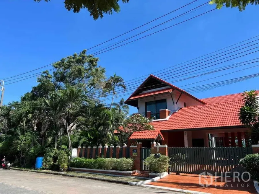 Detached House for rent in Bang Phli, Samut Prakan - Exterior of detached house with red roof, landscaped fence and lush trees under a blue sky.