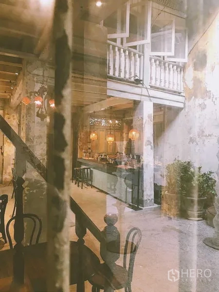 Shophouse for rent in Bang Rak, Bangkok - Double-height shophouse interior with mezzanine balcony, rustic walls and bar area.