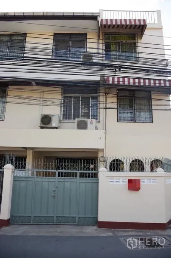 ทาวน์เฮาส์ ให้เช่าในWatthana, Bangkok - หน้าบ้านทาวน์เฮ้าส์ 3 ชั้น มีกำแพงรั้ว ประตูเหล็ก กันสาดลายทาง และแอร์ภายนอก