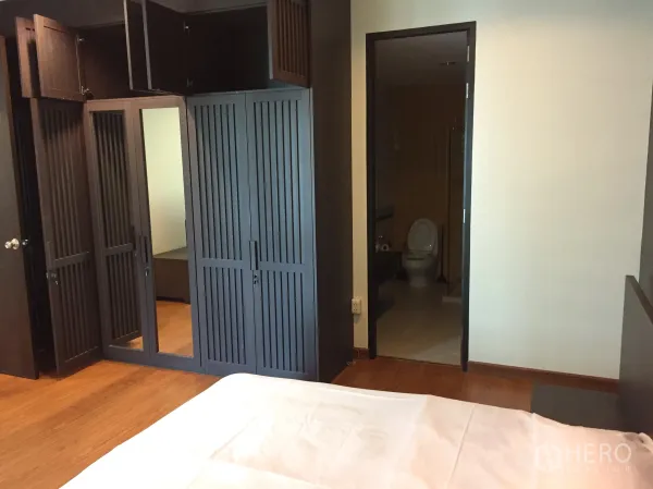 Condominium for rent in Khlong Toei, Bangkok - Bedroom featuring built-in dark wood wardrobes with a doorway to the en-suite bathroom.