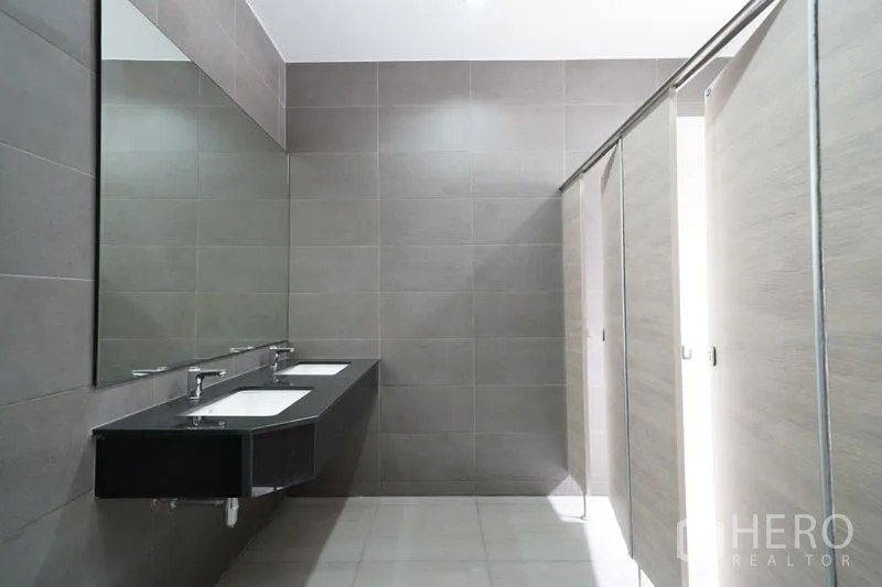 Warehouse for rent in Khlong Luang, Pathum Thani - Modern restroom with long vanity, dual sinks, large wall mirror, and tiled stalls.
